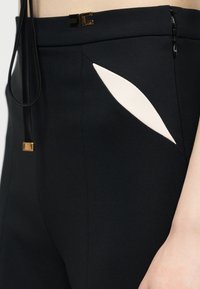 Μαύροι ψηλόμεσοι παντελόνια με λευκή διαγώνια λεπτομέρεια στην τσέπη, χρυσό λογότυπο κούμπωμα στη μέση και μαύρο ρυθμιζόμενο κορδόνι με χρυσό άκρο.