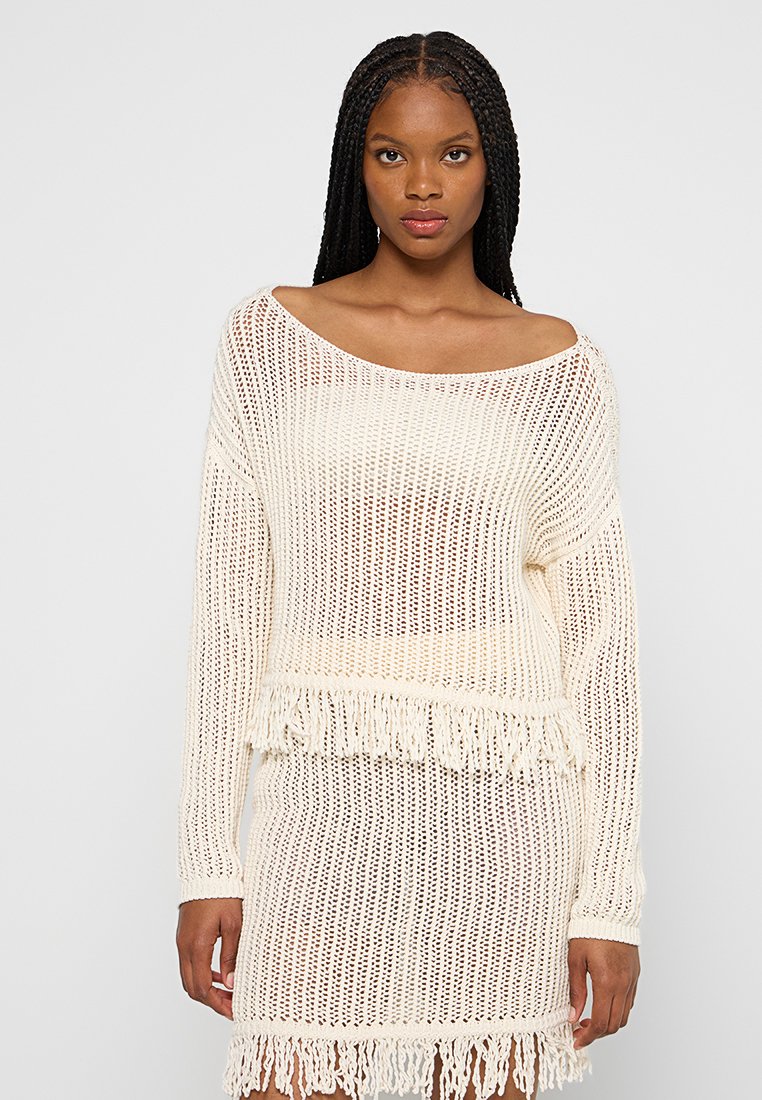 Maglione leggero a spalla scoperta in crema con vestibilità ampia, caratterizzato da una rifinitura a frange sull'orlo. La trama a maglia aperta garantisce traspirabilità.
