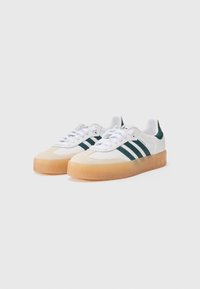 White sneakers with green stripes, rubber gum sole, rounded toe, and smooth texture. Features lace-up closure and logo on tongue.