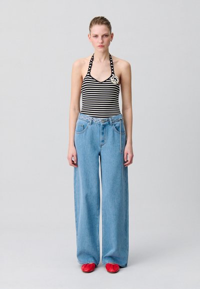 Bañador de cuello halter a rayas combinado con jeans de mezclilla azul claro de pierna ancha y zapatos rojos; presenta un broche decorativo en el bañador.