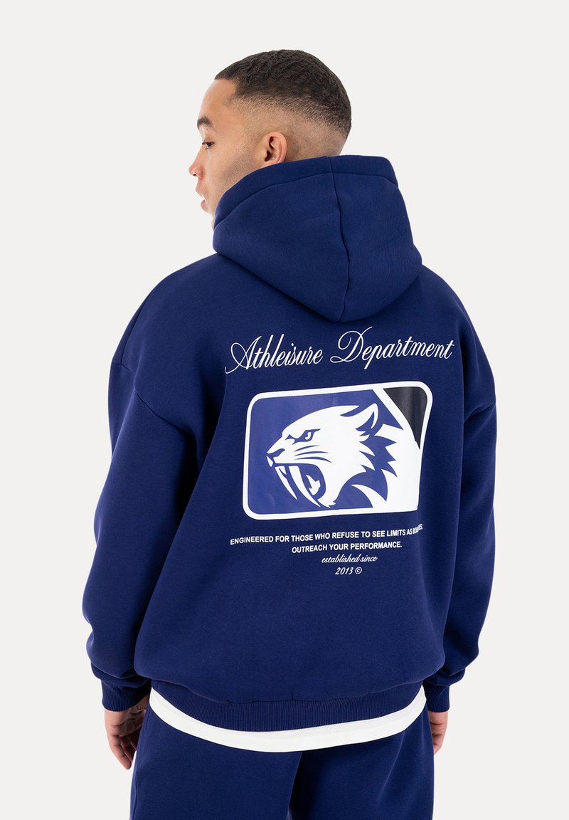 Mann seitlich stehend, trägt einen marineblauen Hoodie mit dem Schriftzug "Athleisure Department" und einer Grafik einer brüllenden Panther auf dem Rücken.