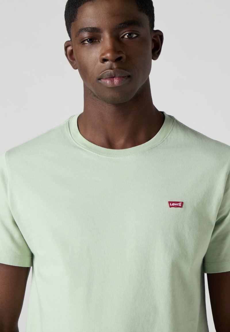 T-shirt en coton vert clair avec un col rond, des manches courtes, et un petit écusson logo rouge Levi's sur la poitrine gauche.