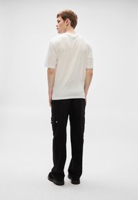 Camiseta blanca de manga corta con un corte holgado, combinada con pantalones cargo negros que incluyen bolsillos laterales y detalles de herrajes plateados.
