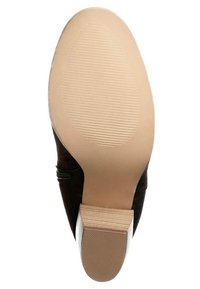 Suela de zapato de ante negro con una suela de goma beige suave y un tacón bajo; cuenta con ranuras horizontales para mayor tracción.