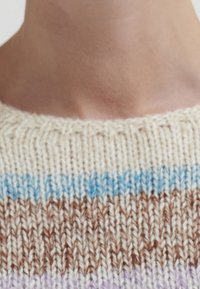 Close-up van de halslijn van een gebreide trui in crème, blauw, bruin en lavendelstrepen op de nek en bovenborst van een persoon.