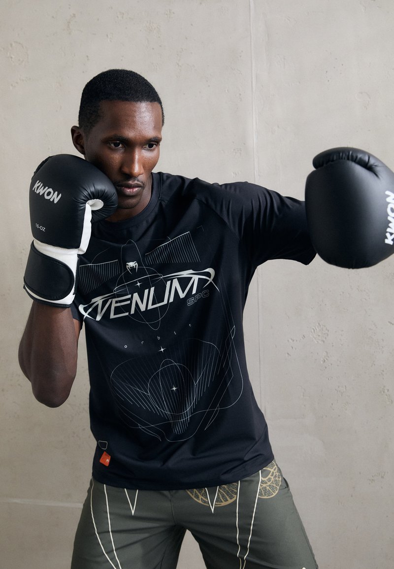 T-shirt de sport noire avec un design graphique, assortie à un short vert olive à motif géométrique. Gants de boxe noirs et blancs.