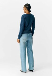 Pull en laine bleu marine à manches longues avec un col rond, associé à un jean droit bleu clair. L'ensemble présente un design minimaliste et des lignes épurées.