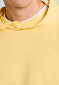 Sudadera amarilla de tela suave, con un cuello acanalado y un sutil logo bordado "PJL" en el frente.