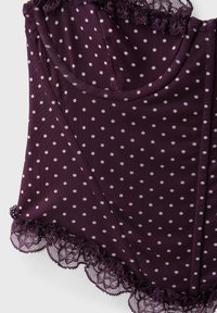 Tissu violet à pois blancs avec une bordure en dentelle le long des bords, plié soigneusement sur une surface plane.