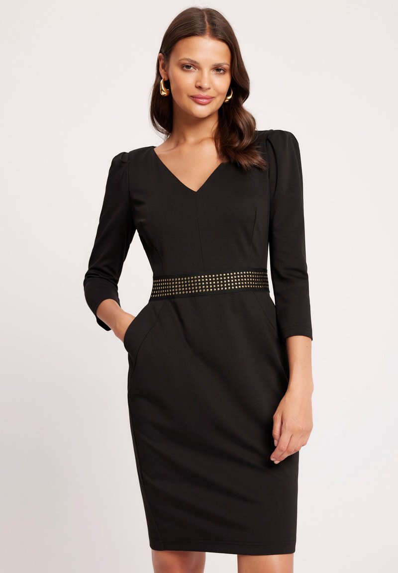Czarna dopasowana sukienka z dekoltem w kształcie V i rękawami o długości trzech czwarte. Posiada teksturowany pasek z metalowymi ćwiekami i boczne kieszenie. Gładka faktura materiału.