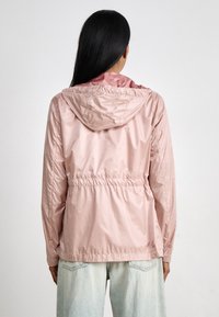 Chaqueta de tejido liso en rosa claro, con capucha, cintura elástica y mangas largas, que presenta una textura suave y un diseño minimalista.