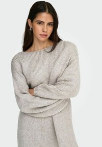Jasnoszary, oversize sweter z szerokim dekoltem, prążkowaną fakturą i długimi rękawami. Miękki dzianinowy materiał z subtelnymi różnicami w odcieniu.