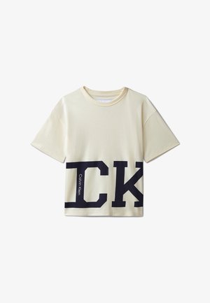 Tricou crem cu mâneci scurte, cu litere mari negre "CK" și text mic vertical "Calvin Klein" în partea de jos a părții din față.