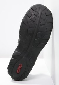 Semelle de chaussure en caoutchouc noir avec des treads profonds et un logo de marque rouge. Présente des motifs de traction variés pour une meilleure adhérence. Design plat et robuste.