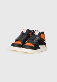 Baskets pour enfants noires et oranges avec une tige en cuir texturé, présentant une sangle Velcro, un collier rembourré et une semelle en caoutchouc blanche.