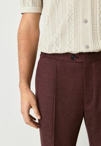 Sweter w kolorze kremowym z krótkim rękawem, z teksturowanym wzorem w diamenty, zestawiony z bordowymi spodniami o dopasowanym kroju z pojedynczym guzikem i bocznymi kieszeniami.