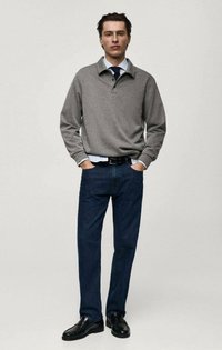 Grå bomullspullover med krage, lagd över en ljusblå skjorta, tillsammans med mörkblå jeans och svarta skor.