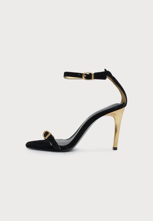 Sandale noire à talon haut et bout ouvert, avec des brides à la cheville et sur les orteils, des boucles dorées et un talon doré métallisé.