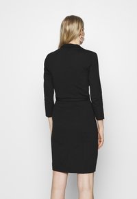 Svart klänning i mjukt tyg med en figursydd design, långa ärmar och en subtil indragning vid midjan, knä-lång.