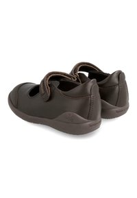 Zapatos de cuero marrón con puntera redondeada, correas de Velcro ajustables y una suela de goma texturizada. Presenta detalles laterales recortados y un branding sutil.