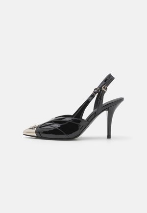 Décolleté in vernice nera con punta affusolata, cappuccio dorato metallico e sottile tacco a stiletto; presenta un design di cinturino incrociato.