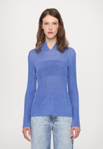 Suéter de punto acanalado azul con una silueta ajustada, que presenta un escote en V y mangas largas, combinado con unos jeans desgastados de tono claro.