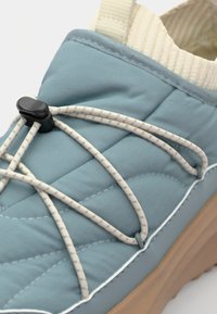 Blå quiltete sneakers med teksturert finish, med elastiske snørebånd, en svart toggle og en beige gummisåle.