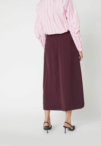 Pantalones de pierna ancha en burdeos con un tejido suave, cintura alta y frente plisado, combinados con una blusa rosa a rayas y tacones negros.