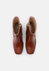 Bottines en cuir marron à finition lisse, bout carré, fermeture éclair latérale et semelle en caoutchouc noire. Le nom de la marque "RAID" est visible à l'intérieur.