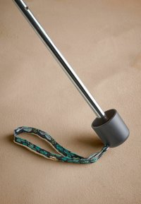 Fém bot szürke gumitippel és teal virágmintás anyagpánttal, egy semleges felületen pihen.