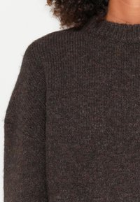 Ciemnobrązowy sweter z dzianiny o teksturowanym wzorze, z prążkowanym dekoltem i luźnym krojem. Materiał wydaje się miękki i puszysty.
