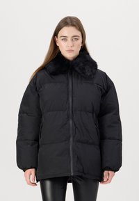 Black puffer jacket featuring a faux fur collar, zip front, and elastic cuffs. The design is oversized with a quilted texture.