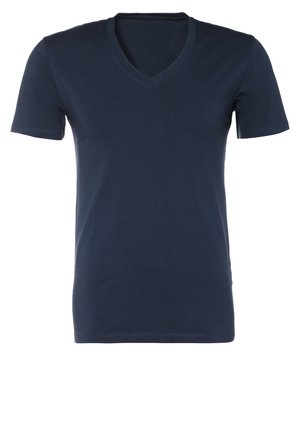 Homme marchant vers l'avant portant un t-shirt bleu marine à col en V, un jean gris clair, des chaussures noires, une ceinture marron, une montre-bracelet, portant un sac de sport beige sur l'épaule.