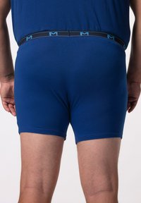 Boxer shorts di cotone blu scuro con una vita nera che presenta un logo blu. Il tessuto è liscio e si adatta perfettamente alle cosce.