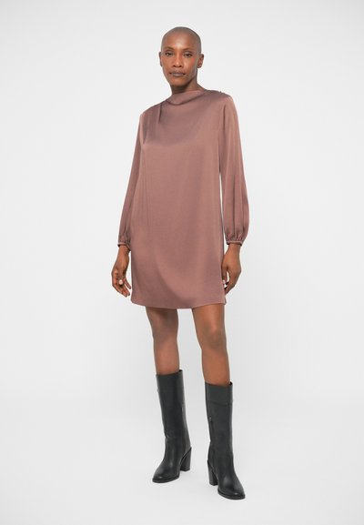 Robe en satin marron à manches longues et longueur genoux avec un col haut et des manches froncées, portée avec des bottes noires à talons montantes.