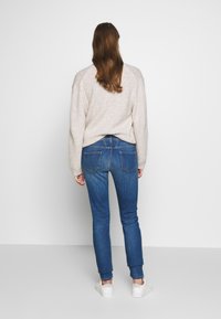 Light beige sweater, mid-rise blue jeans, slim fit, smooth texture; white sneakers, subtle blue stitching on jeans, back view.