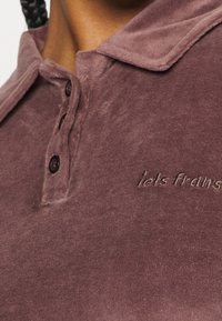 Hladký, tmavě fialový polo shirt s měkkou strukturou, který má límeček, tříknoflíkovou légou a vyšitým logem v tmavší odstínu.