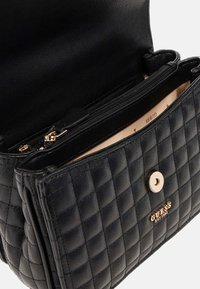 Bolso de mano de cuero acolchado negro con cierre de botón dorado y un bolsillo interior con cremallera. El forro es de un beige claro con detalles del logotipo de la marca.