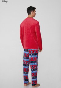 Rotes, weiches Samtoberteil mit langen Ärmeln, kombiniert mit blauen, gemusterten Pyjamahosen, die Stitch, Weihnachtsmotive und festliche Farben zeigen.