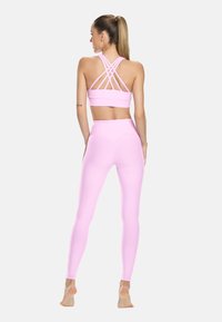Světle růžový sportovní podprsenka s křížovými ramínky na zádech, kombinovaná s legínami s vysokým pasem ve stejném odstínu, vyrobenými z hladké, elastické látky.