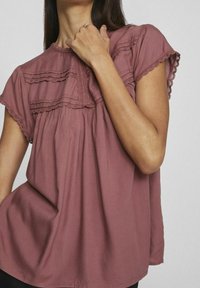 Blusa in cotone prugna con maniche a cappuccio corte, bordo in pizzo, dettagli arricciati e vestibilità ampia. Tessuto morbido con una leggera lucentezza.
