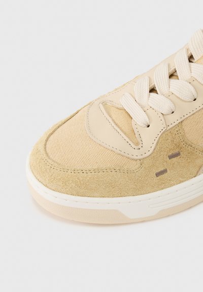 Μπεζ αθλητικό παπούτσι με μείγμα από σουέτ και υφασμάτινα υλικά, στρογγυλεμένη μύτη, επίπεδη λευκή σόλα και υφασμένες κορδόνια. Υποτονικές λεπτομέρειες στο πλάι.