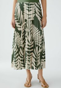 Jupe plissée verte avec des motifs de feuilles beiges, dotée d'une taille élastique. Le tissu a une texture lisse et tombe jusqu'au mollet.