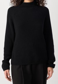 Pull noir côtelé avec un col haut et des manches longues. Présente un motif de tricot texturé et une coupe décontractée. Assorti à un pantalon sombre.