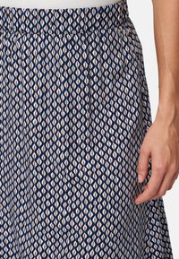 Jupe marine avec un motif géométrique en blanc, bleu clair et brun, dotée d'une taille élastique et d'une texture de tissu lisse.