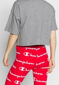 Grå t-shirt med kort ärm, kombinerad med röda leggings som har ett vitt repetitivt "Champion" logotypdesign.