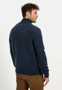 Granatowy sweter z dzianiny z wysokim kołnierzem, ściągaczami przy mankietach i u dołu, z charakterystyczną struktura w drobne plamki oraz wyraźnymi szwami na ramionach.