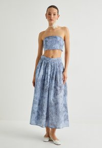 Blaues zweiteiliges Outfit mit einem trägerlosen Cropped-Top und einem plissierten Maxirock, gefertigt aus strukturiertem Stoff mit floralen Mustern.