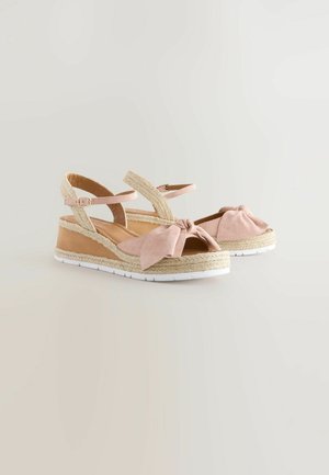 Růžové semišové klínové sandály s uzlovou mašlí, střední část obalenou jutou a nastavitelnými pásky kolem kotníku. Bílá gumová podešev pro lepší přilnavost.
