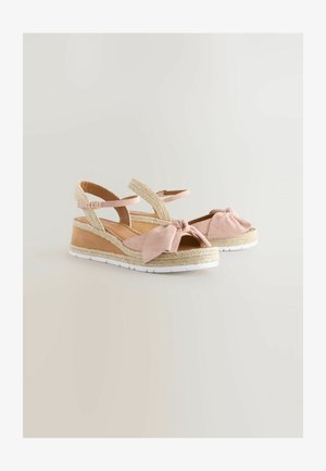 Růžové semišové klínové sandály s uzlovou mašlí, střední část obalenou jutou a nastavitelnými pásky kolem kotníku. Bílá gumová podešev pro lepší přilnavost.